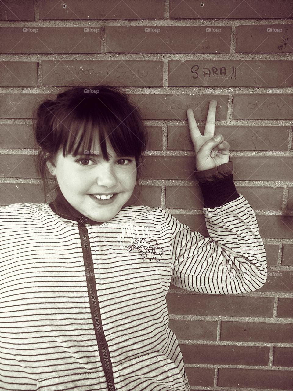 Portrait of smile girl standing against brick wall gesturing