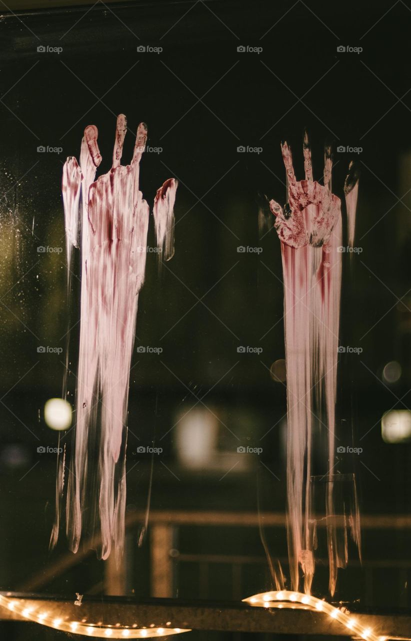 Bloody traces of adult hands with smearing on the glass of the window at the night of Halloween celebration, close-up side view. Halloween concept.