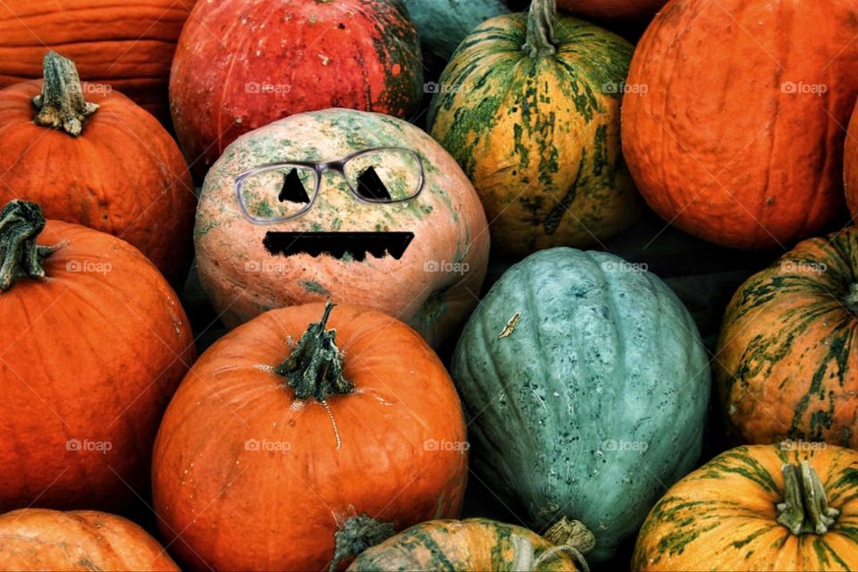 Full frame of many orange and green pumpkins and one is wearing glasses and a painted face