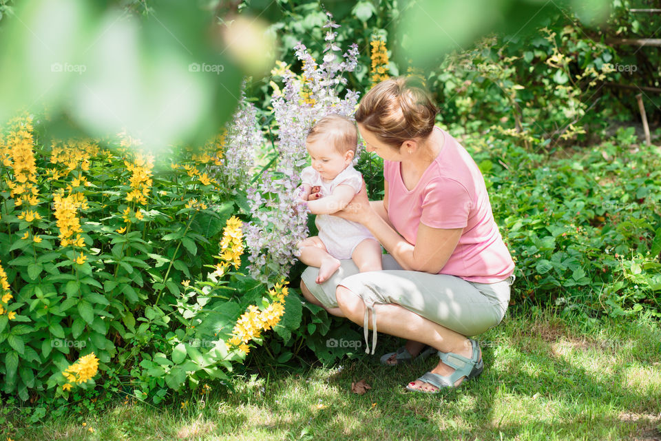 Mother with baby in the garden. Mother showing the garden plants her baby girl