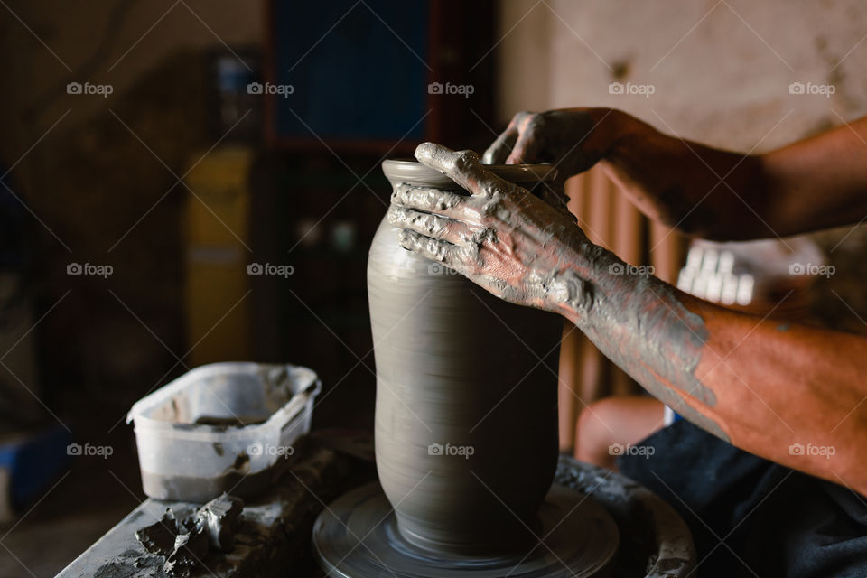 Close-up on hands of craftsman while working clay pot in his workshop