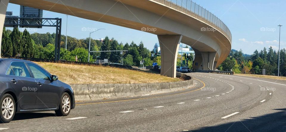 black car driving down the street under an overpass bridge on a sunny day in Oregon