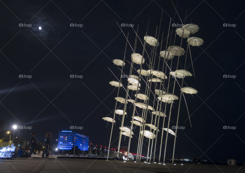 Virtual umbrellas art on the seafront by the moon at night in Thessaloniki, Greece .