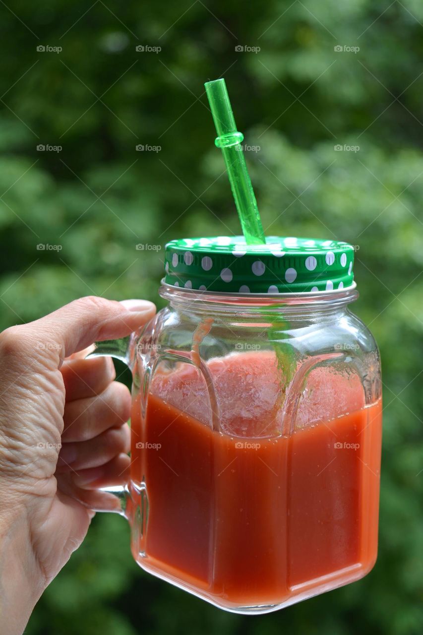 tomatoe juice in cup in the hand green background, healthy food, lifestyle