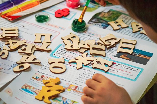 A boy with his mother paints wooden letters in different colors.