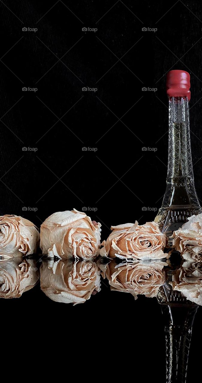 Some roses and a bottle reflected in the water on a dark background 