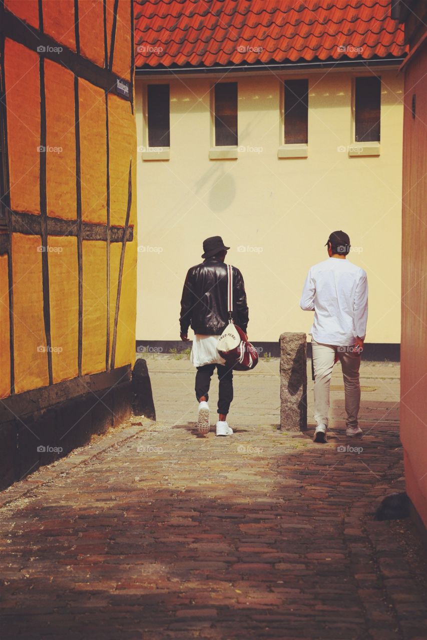 Two men in the back street. Taken in a backstreet in Denmark . The houses are different shades of yellow and the streets are made of cobblestones 