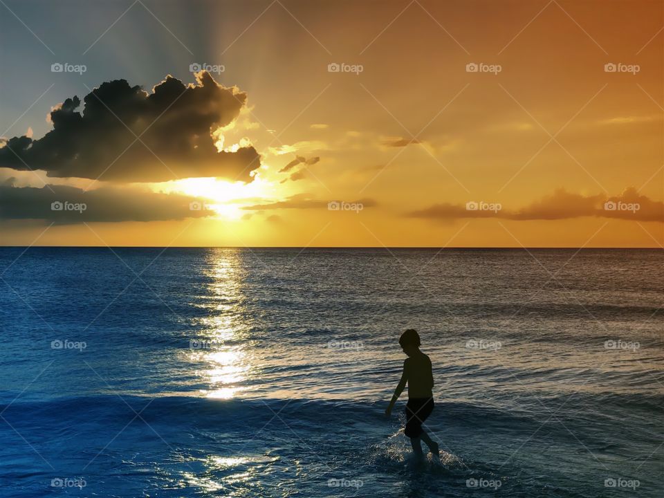 Small boy in the big blue ocean under a spectacular golden sunset.