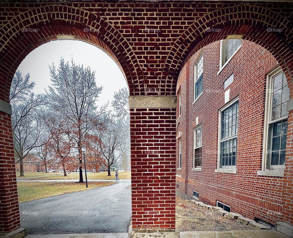 A double brick archway on a college campus looks into the courtyard.