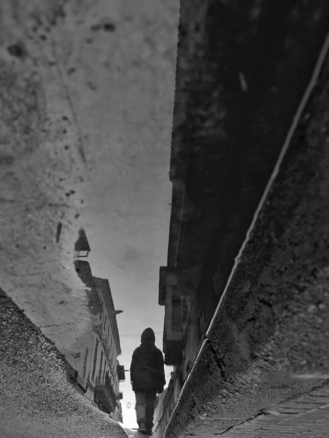 Inverted reflection of a child walking down on a rain-wet street.