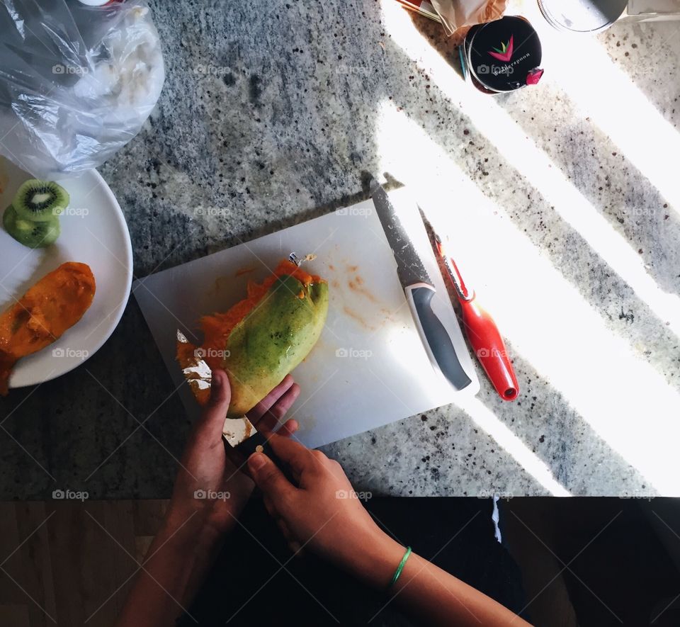 Person cutting mango fruit on cutting board