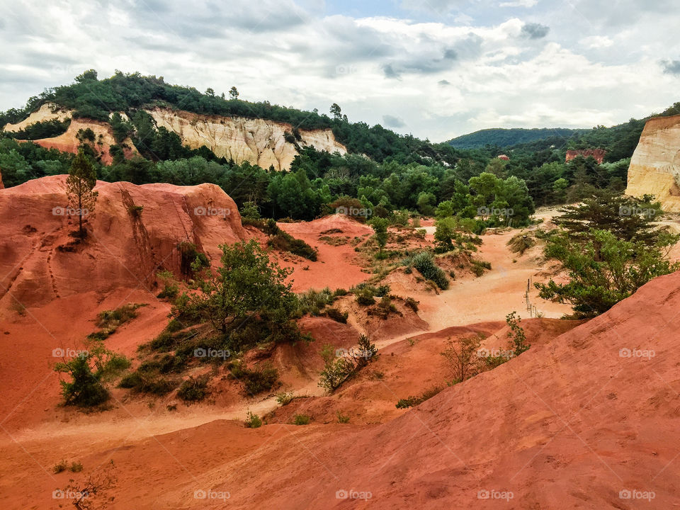 Nature reserve called Colorado Provencal in France with trees and orange colored sand dunes high as mountains a rainy day in summer.