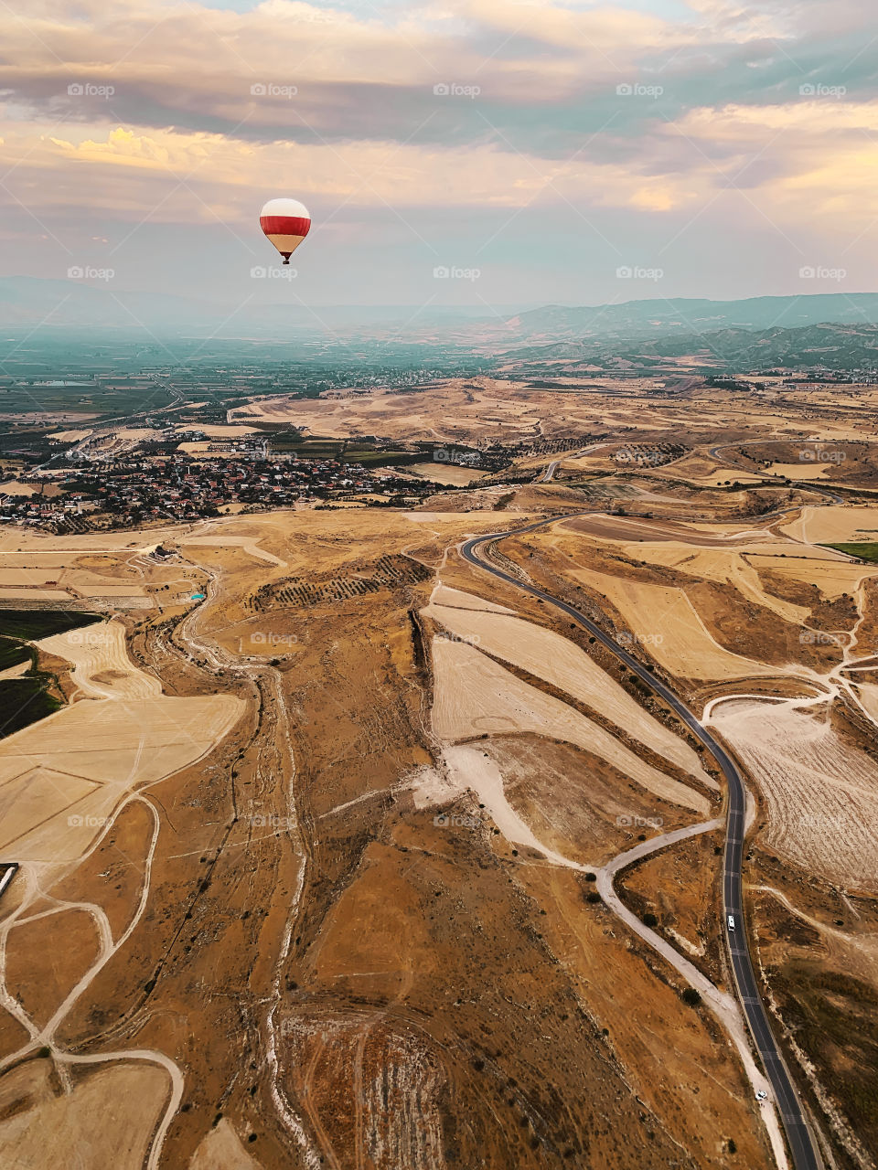Hot air balloon flying over the beautiful landscape with open road 