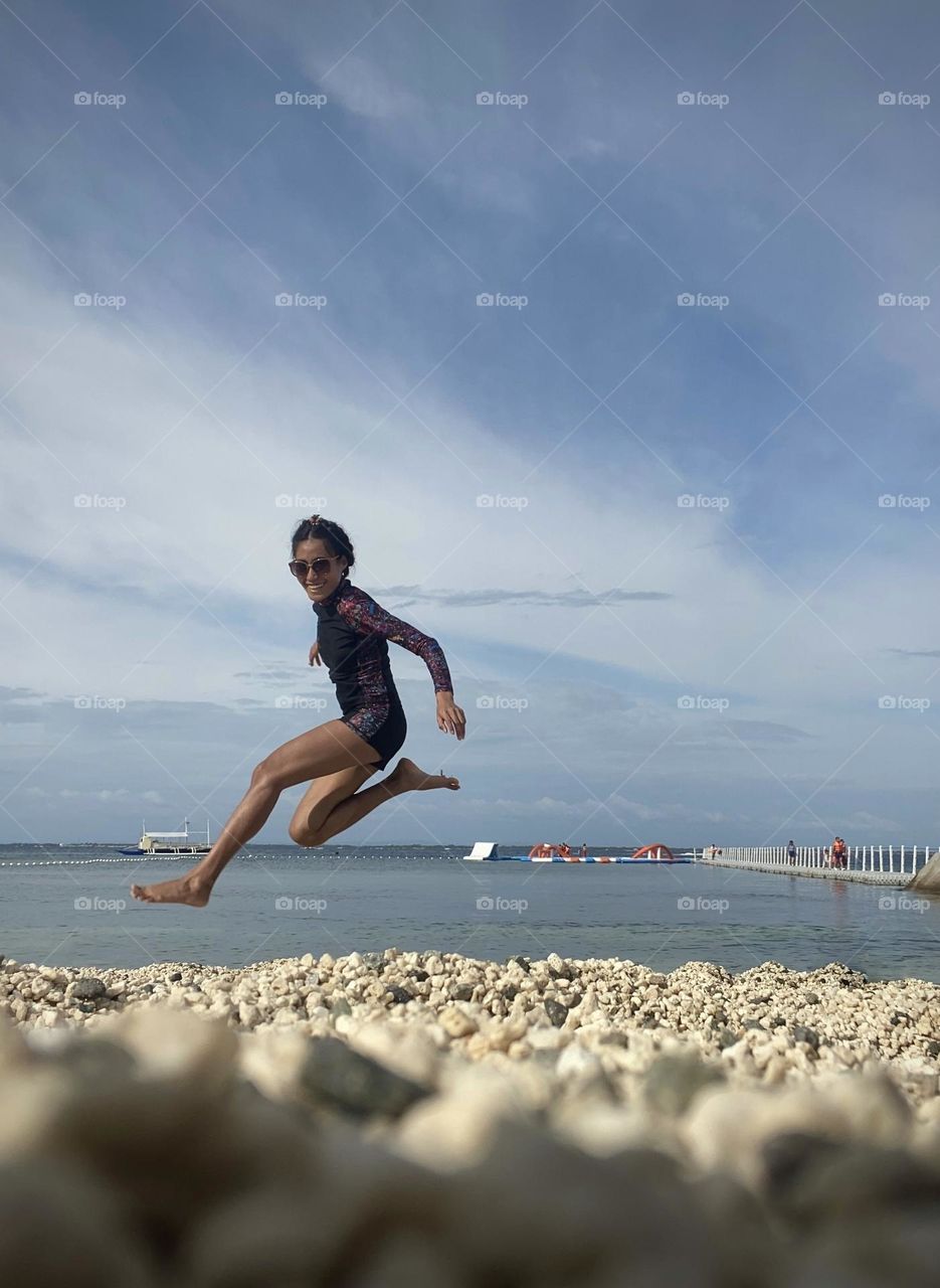 A woman enjoying jumping on the seashore. On a sunny beautiful day, Philippines.