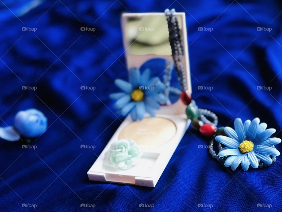 A beauty product with blue flowers and colourful pearl chain on blue satin cloth