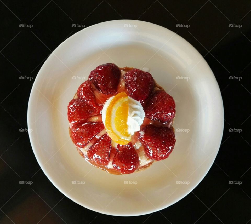 sweet with cookie, strawberries, orange and cream on a plate from top