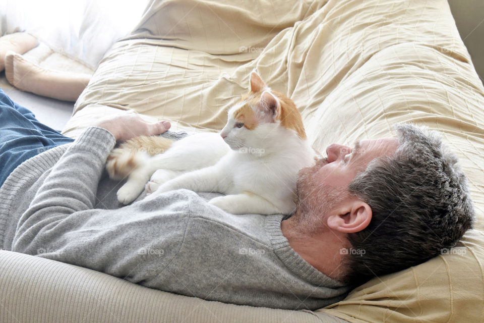 Cat laying on owner's chest. Cat and owner sitting together on the sofa at home.