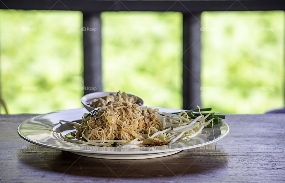 Fried noodle with spring onion and bean sprouts on white plate with garnish.