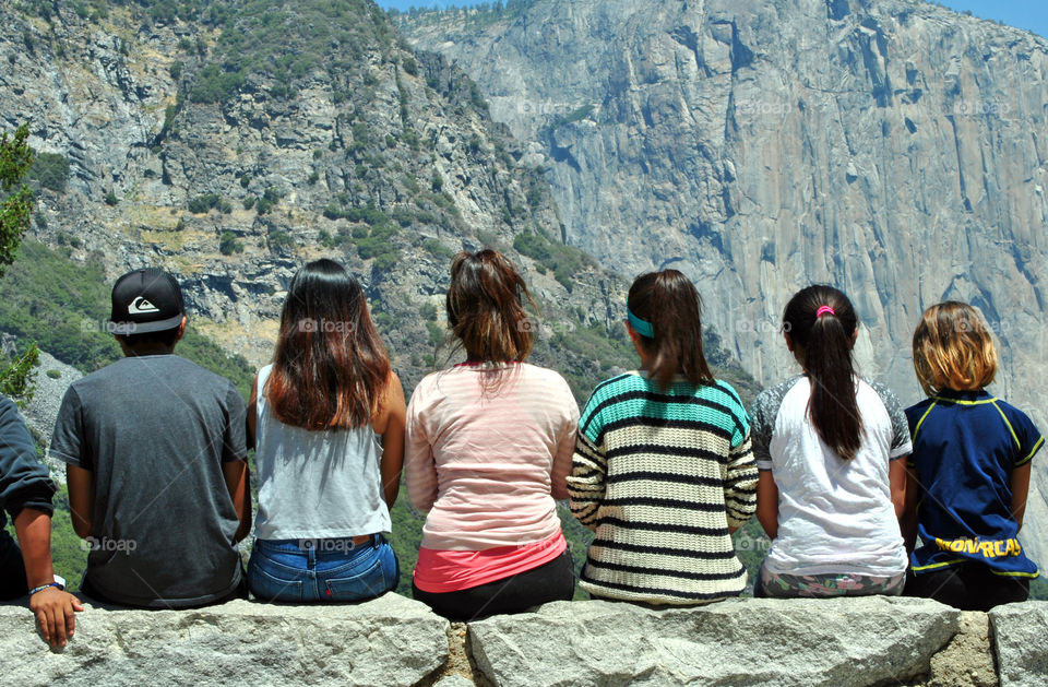 group of people, most likely teenagers, sitting in one row, looking at the beautiful view of Yosemite mountain, national park, taken behind their back