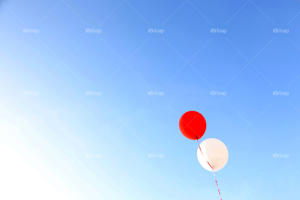 Red balloon and white balloon drifting upwards to the heavens of blue and white skies 