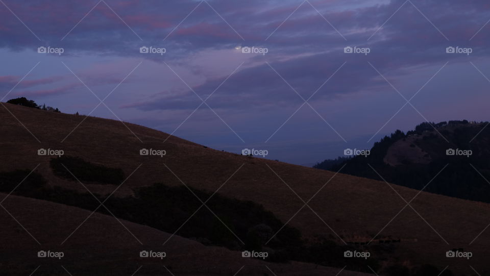 Moon hiding behind clouds in a purple sky