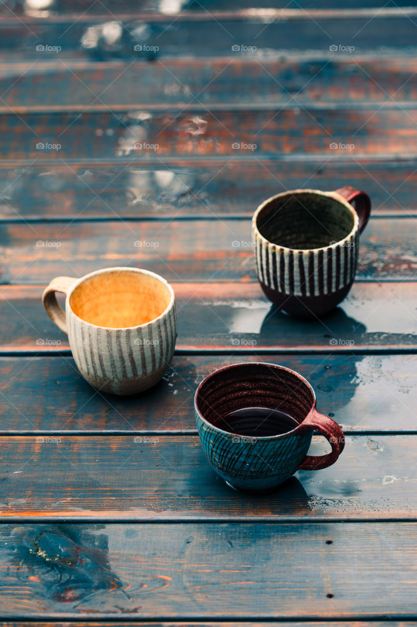 A couple of earthen cups with coffee and herbal tea on wooden wet table after rain