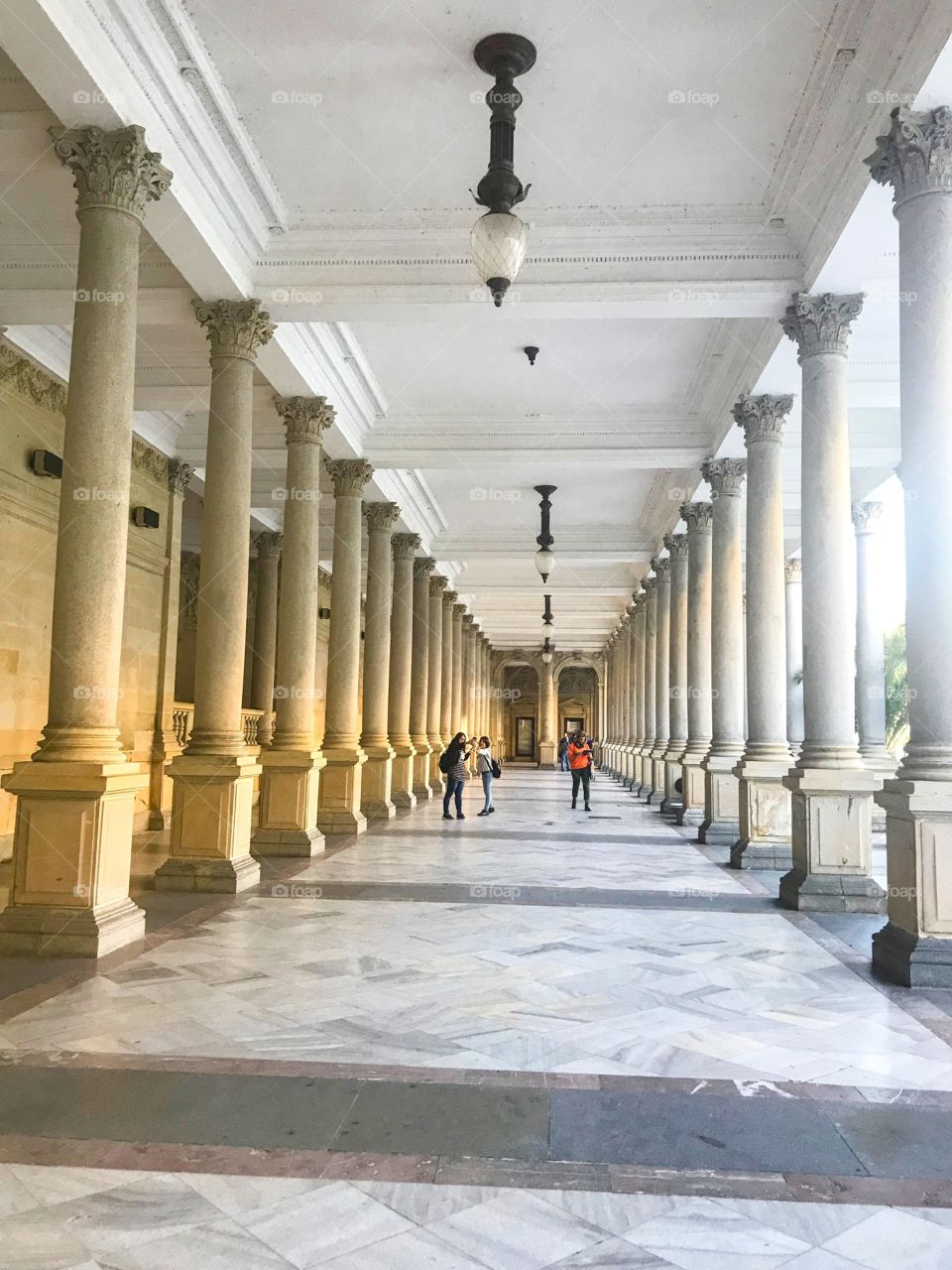 colonnade ,on the ceiling there are some old fashioned lamps,some people are visit,taking picture. The architecture is impressive