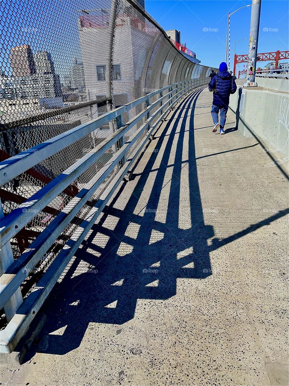 This is the pedestrian lane of the “Pulaski Bridge” at “Newtown Creek” that connects “Greenpoint”, Bklyn to LIC, the direction we are facing. The shadows cast by the bridge’s railing concoct intricately interwoven patterns. 2024. Hypnotic Productions