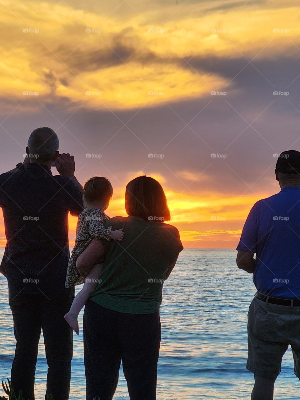 A family with a very young child enjoys the beauty of a spectacular sunset over the Pacific Ocean in Southern California