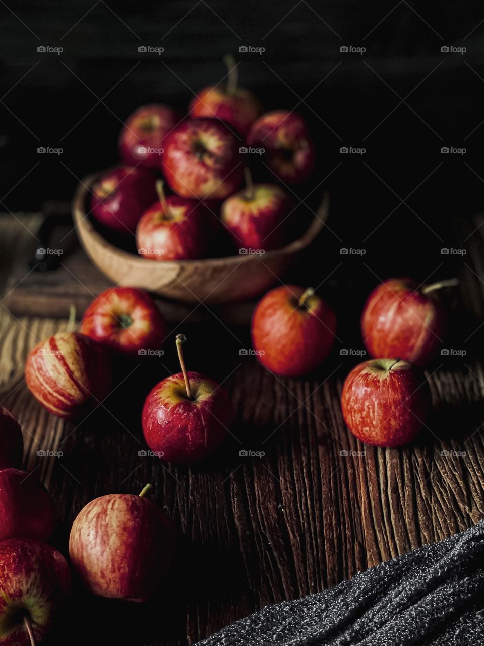 Scattered red apples on a wooden table and some in a wooden bowl