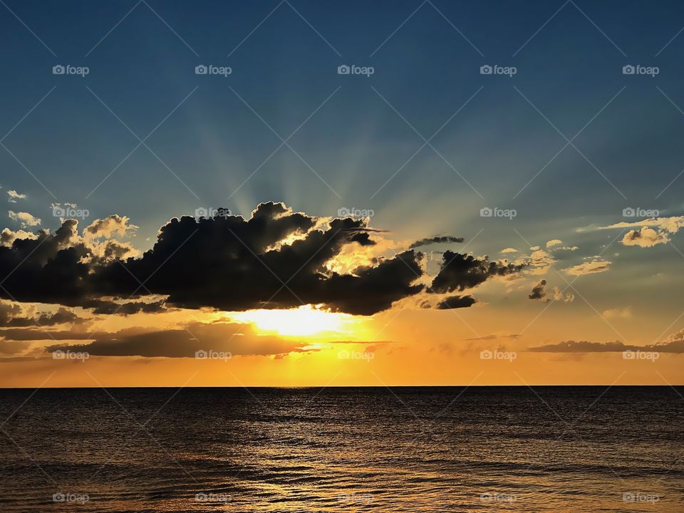 Dark clouds shroud a brilliant golden ocean sunset.