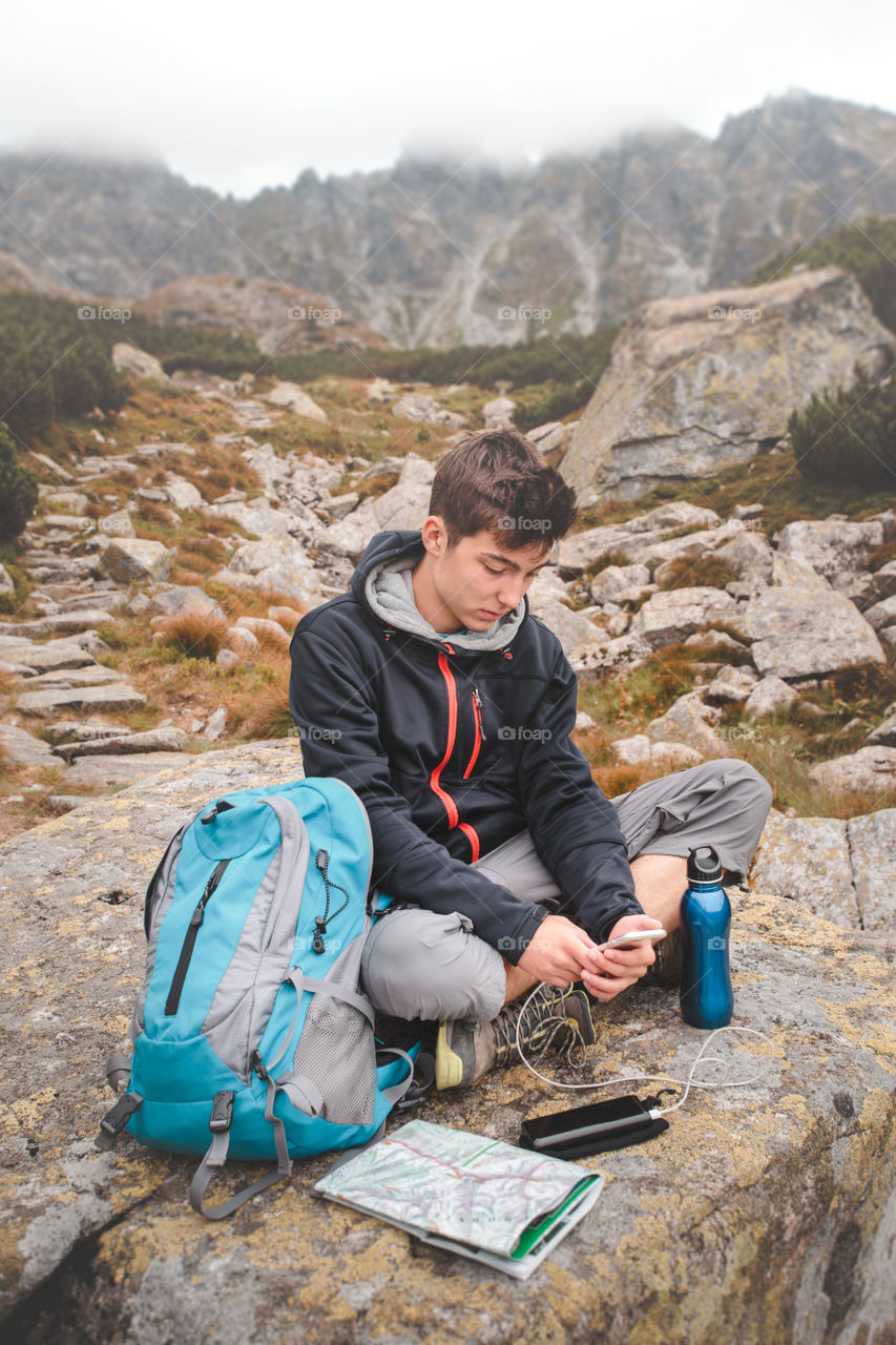 Teenage boy sitting on rocks using mobile phone