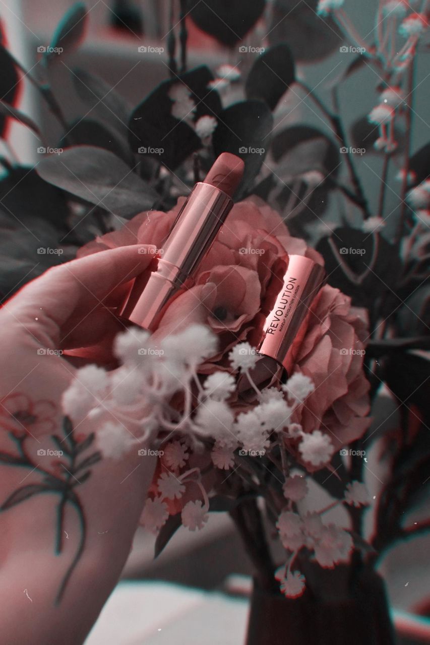Lipstick in a hand around flowers