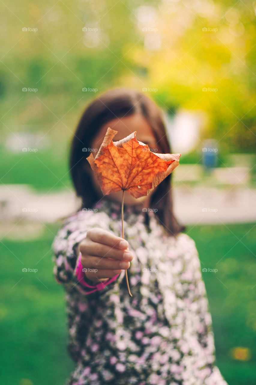 Girl holding a dry leaf in front of a her face