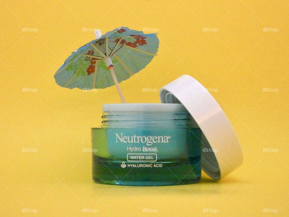 Bottle of cooling and hydrating Neutrogena Hydro Boost water gel face lotion on a yellow background with a tropical umbrella