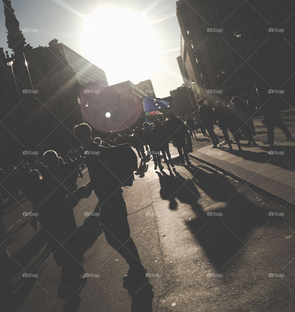 A busy London street following a protest, the sun is going down creating long shadows.