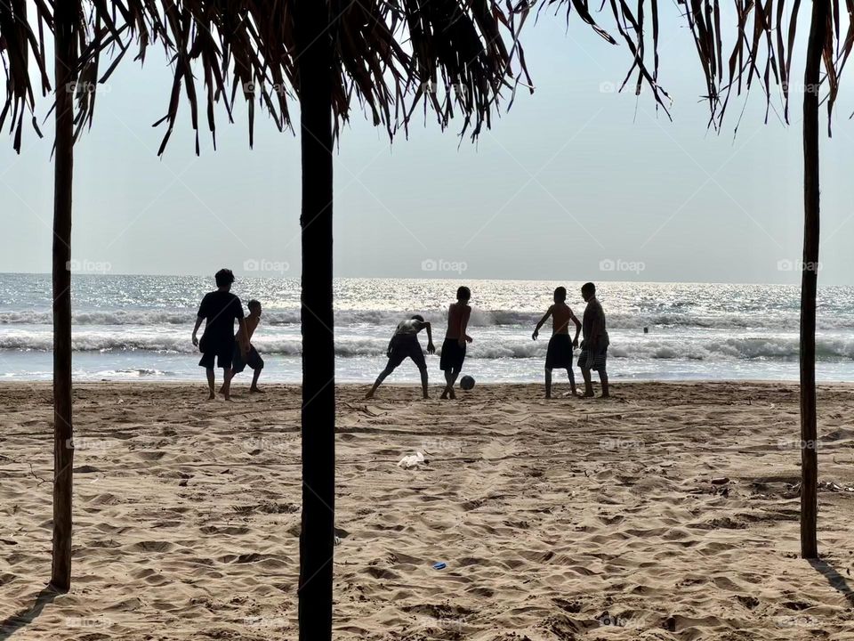 Boys having fun playing football soccer on the beachfront in a warm and sunny day.