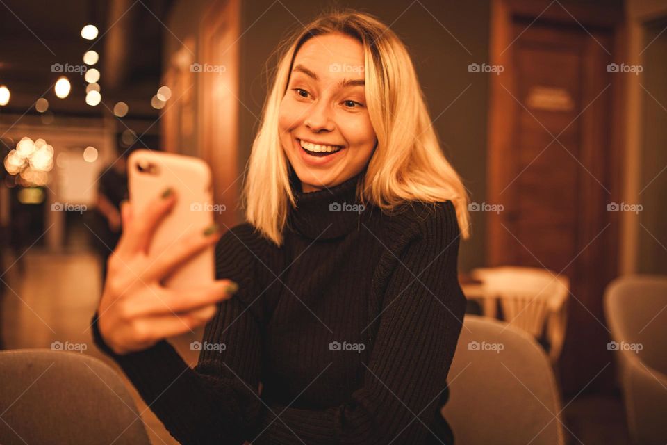 beautiful young woman is sitting in a cafe.  blonde speaks on the phone.  happy woman