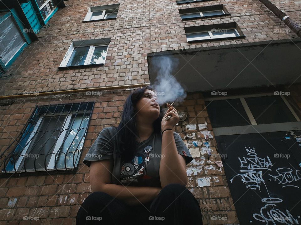 Portrait of a smoking girl against the background of rectangular windows of a house