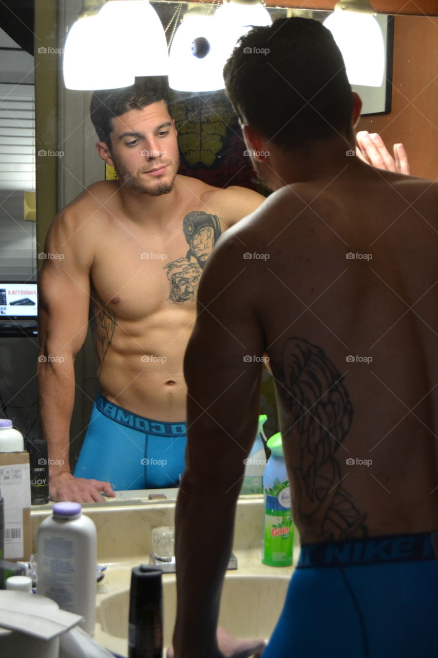 Handsome man looking tattoo in his body through the mirror