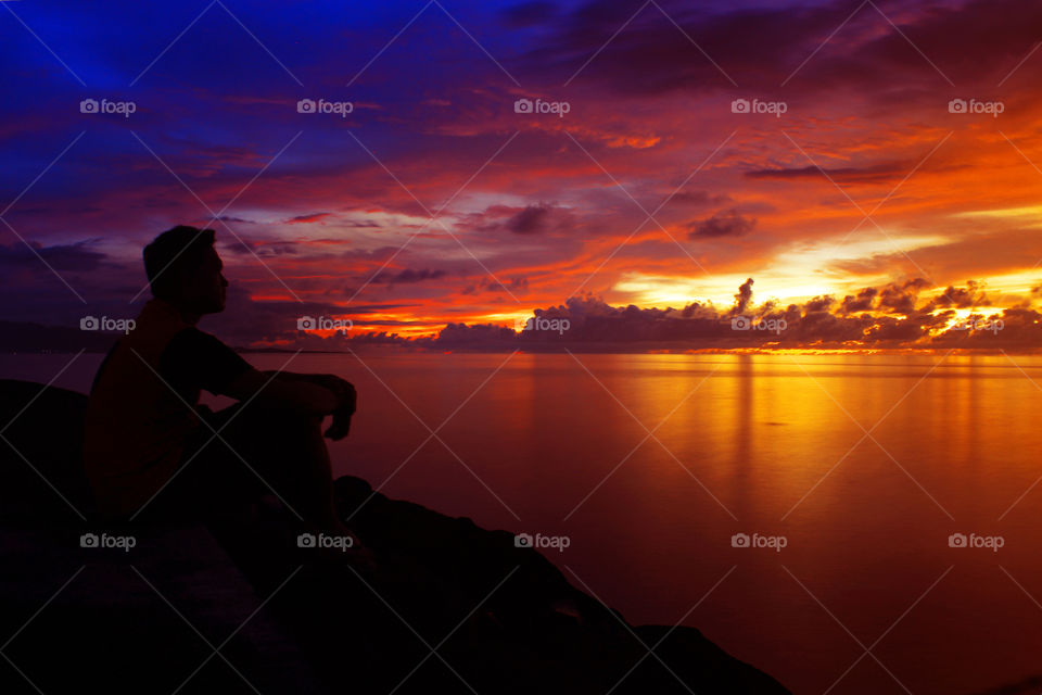 Silhouette of a person sitting near sea at sunset