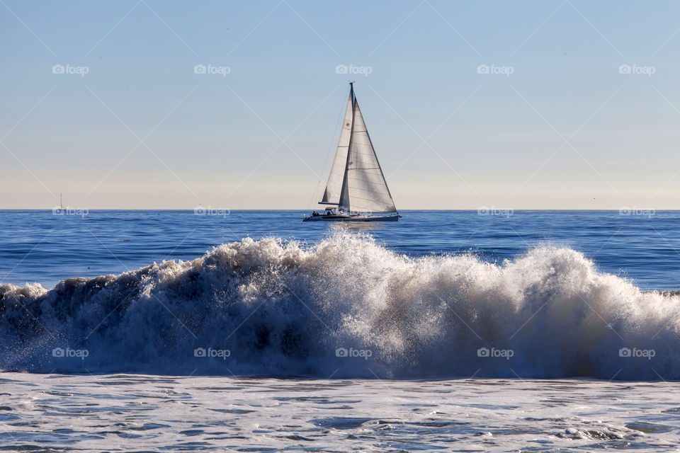 Waves crushing at the beach in San Francisco with sailing boat at the distance