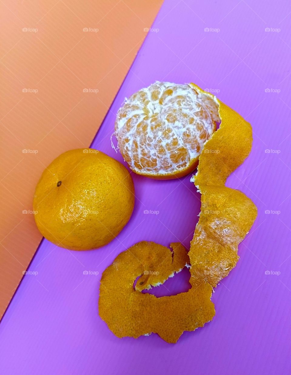 a whole Mandarin orange and a half peeled Mandarin Orange on orange and pink background.