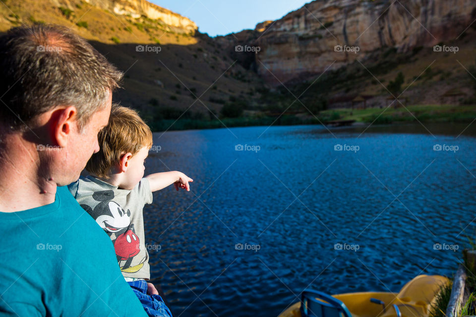 Dad and his son looking to the lake and mountains at sunset. Boy pointing to the distance. Love this family moment of sandstone mountains in Clarens South Africa