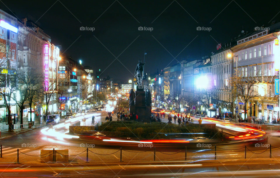 Wenceslas square with long traffic lights late autumn evening by Museum of cockroaches with a focus on monument Wenceslaus. People whose faces cannot recognize, going to the  circle and having fun.