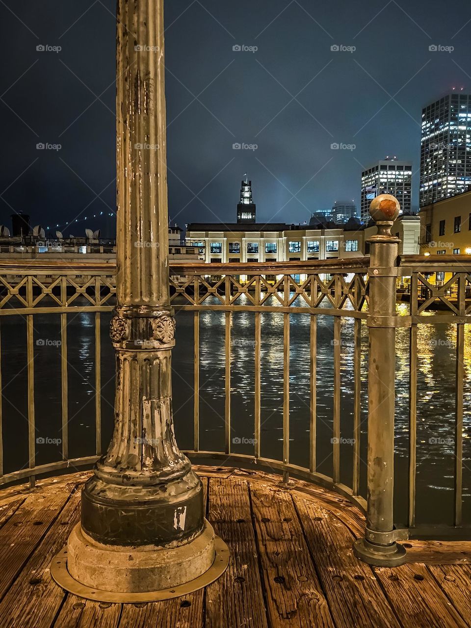 Night view of San Francisco looking through the railing at pier 7 on the waterfront with a slight bit of fog and the lights reflecting in the water