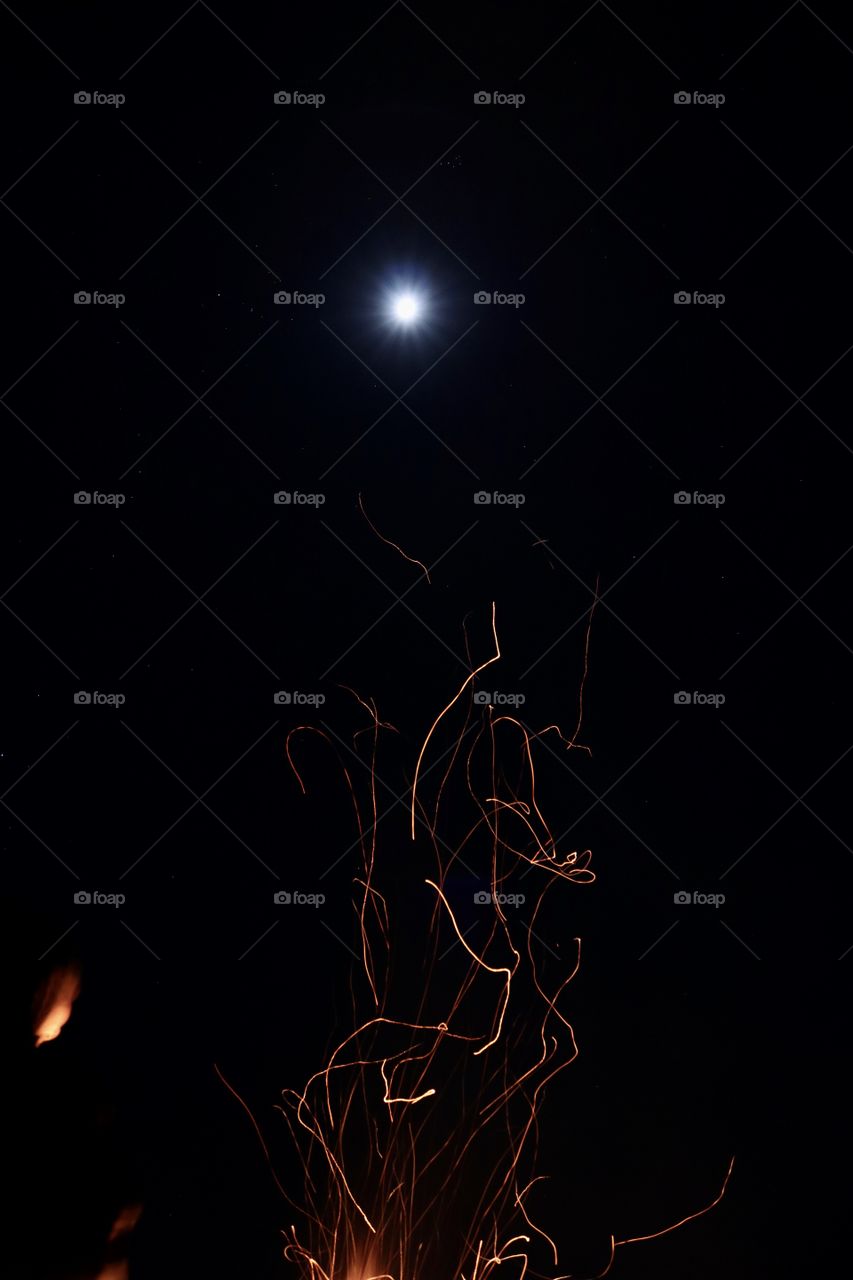 Sparks from a fire swirling up towards a full moon.