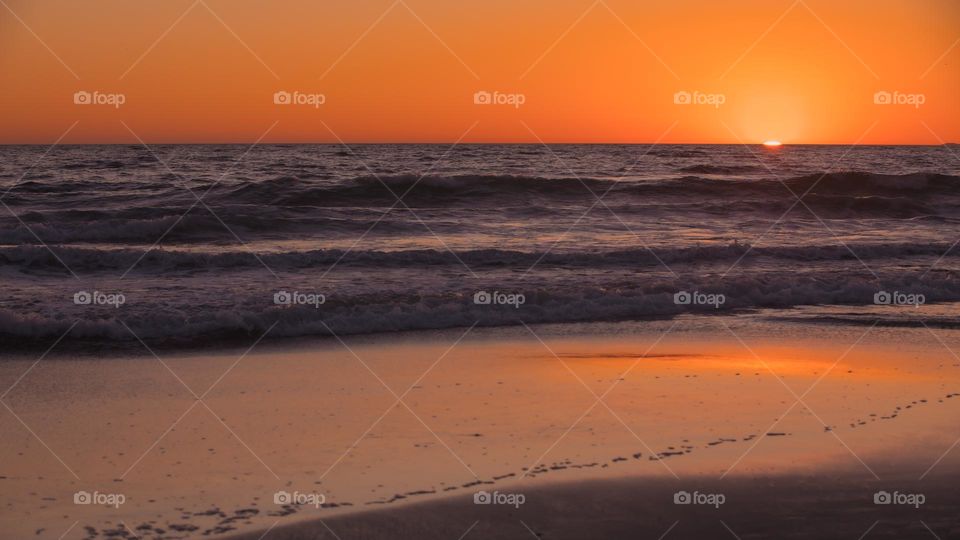 Last moments of sun setting into water horizon at Santa Monica Beach in Los Angeles, California, USA. Warm orange light from the sun reflect onto sea surface. April 2022. Inspiring view.