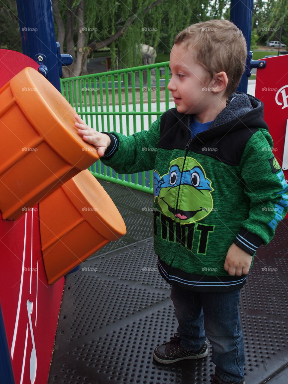 A little boy enthusiastically plays on the plastic drums on a play structure in the park. 