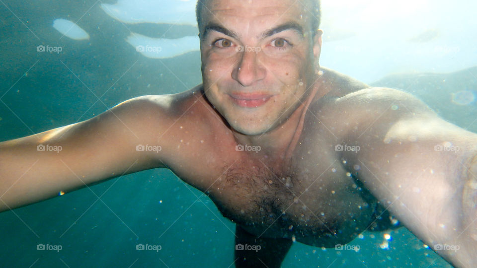 Man diving in the ocean, male underwater smiling,swimming and relaxing in big blue sea with his waterproof camera